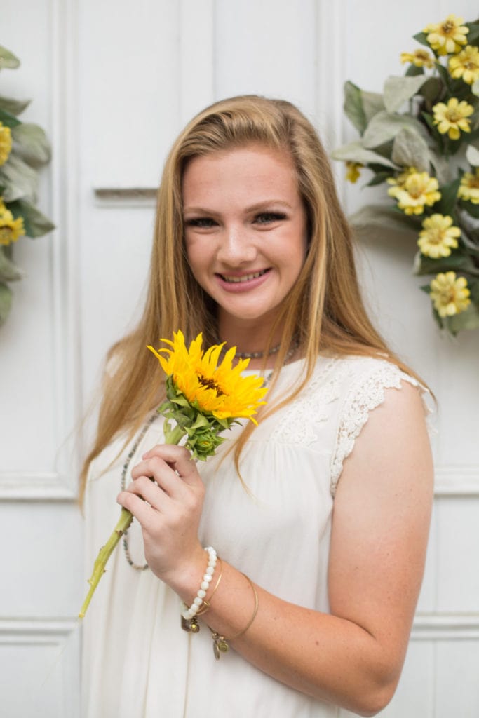 Family Photography - high school girl stands in front of door holding a sunflower